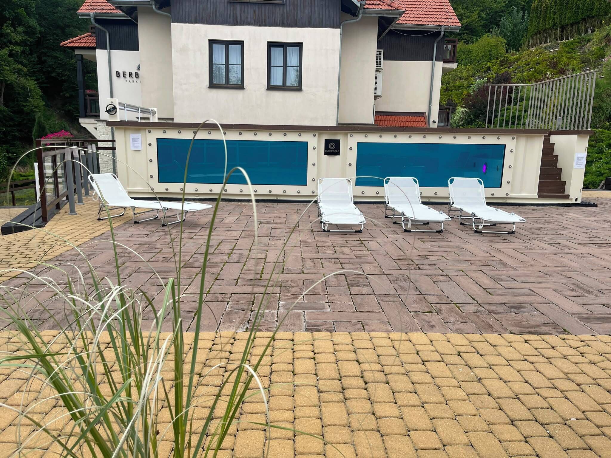 Un área de piscina con sillas de descanso, un edificio con un letrero y una escalera.