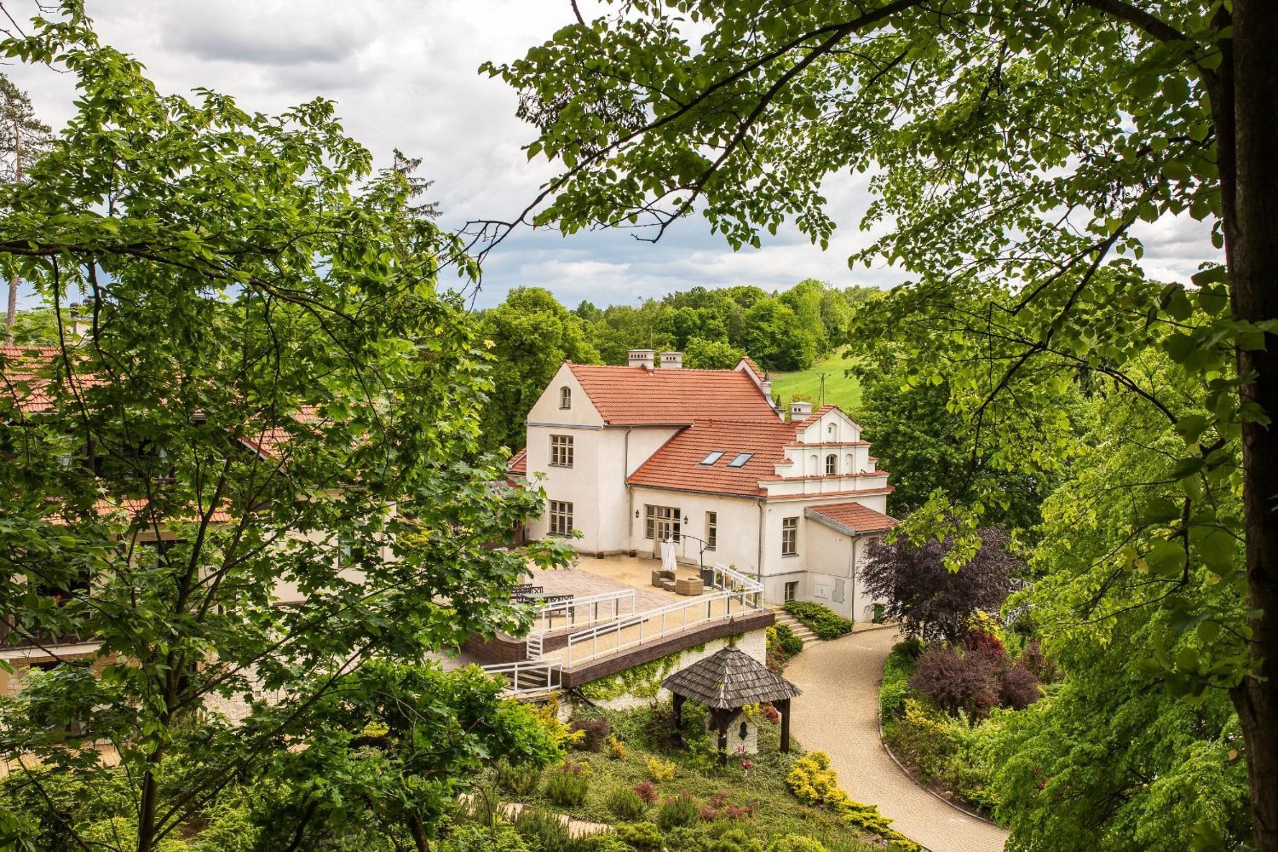 Un grand bâtiment blanc, surmonté d’un toit rouge, entouré d’une végétation luxuriante et bordé d’un chemin pavé.