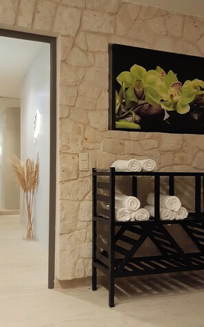 A room with a stone wall, a black console table with rolled towels, and a framed picture of orchids. - Hotel Berberys (Kazimierz Dolny)