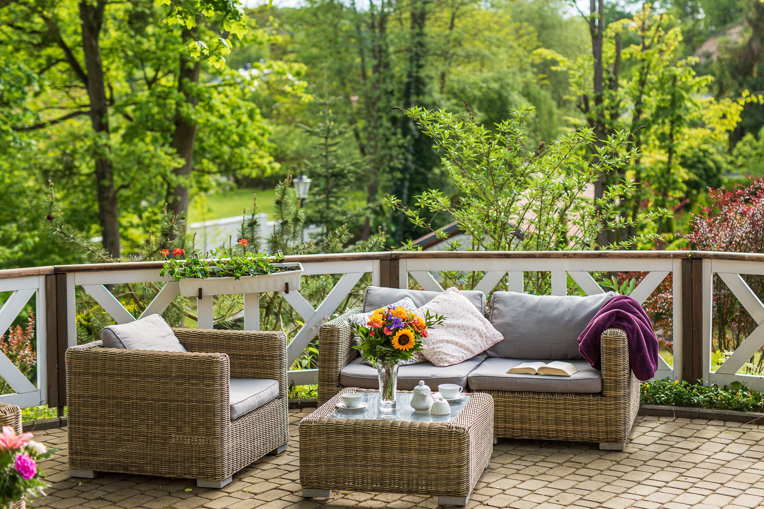 An outdoor seating area with wicker furniture, a glass table, and a vase with flowers.