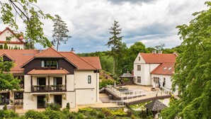 Un hotel con fachada de piedra, techo de tejas rojas y balcón con mobiliario para exterior.