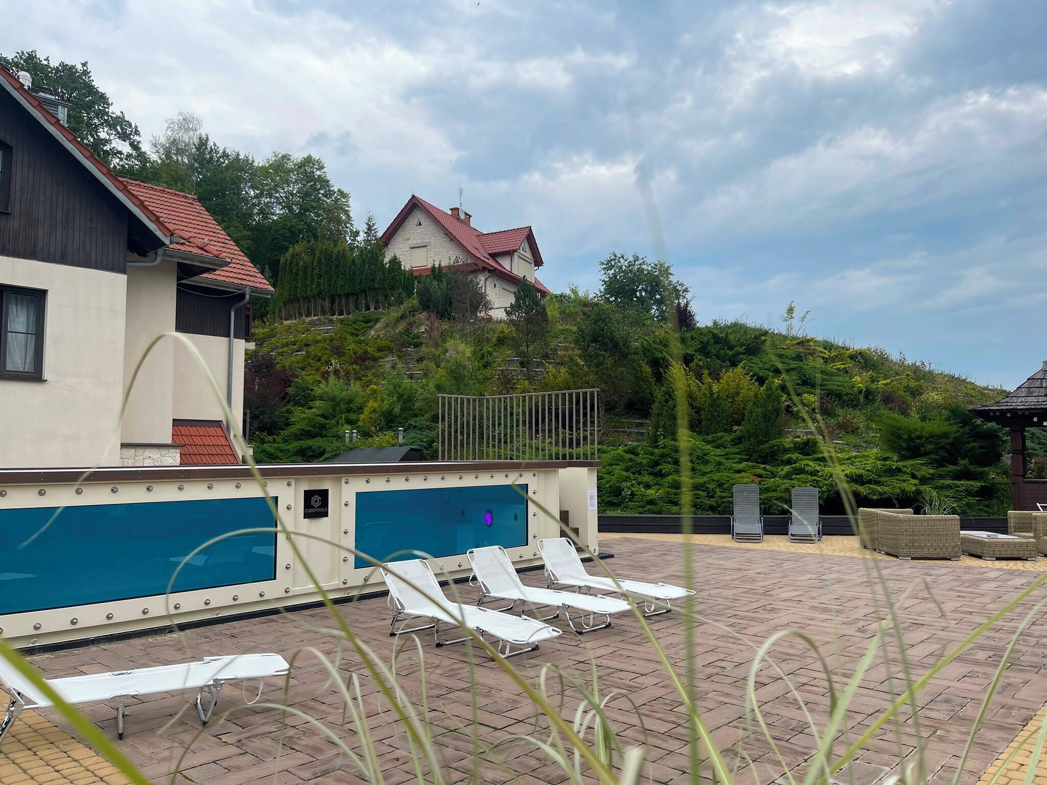 A pool area with lounge chairs and a pool table, surrounded by a landscaped garden and a hillside.