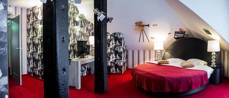 Una habitación de hotel moderna con alfombra roja, una cama con cubrecama rojo, un escritorio con televisor de pantalla plana y una pared con proyector de películas y un letrero que dice 'START DIRECTOR'.