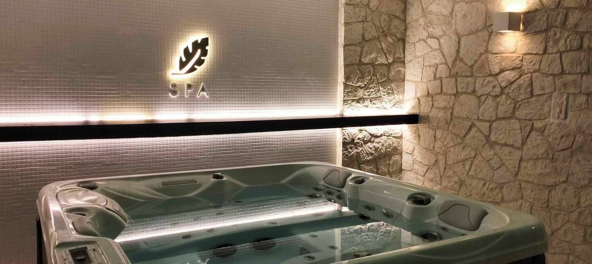 Área de spa com hidromassagem, parede de pedra e placa com a palavra 'SPA' iluminada.