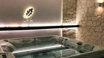 Área de spa com hidromassagem, parede de pedra e placa com a palavra 'SPA' iluminada.