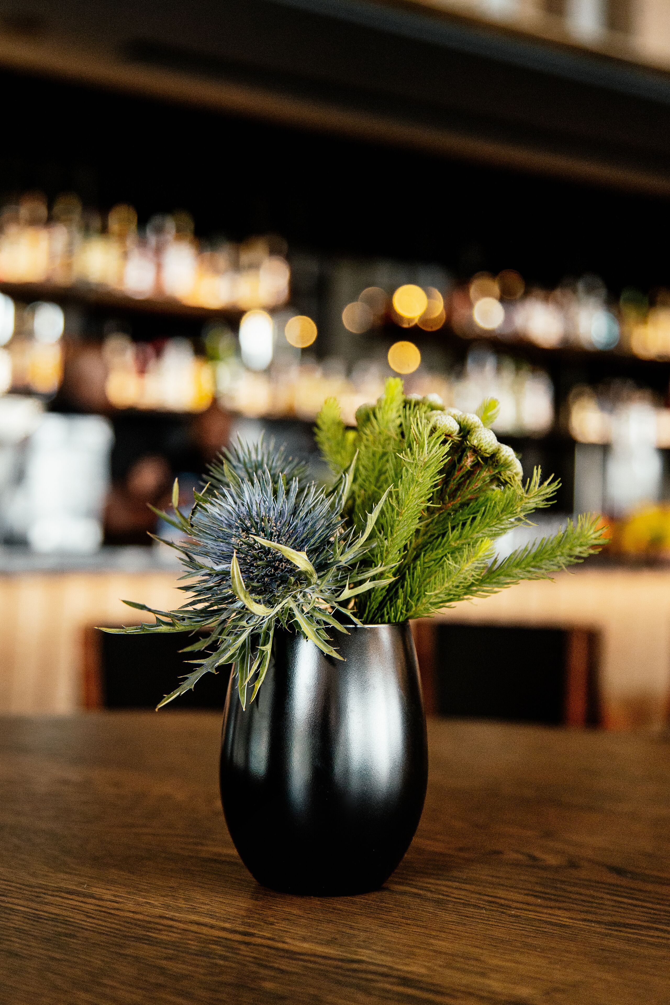 Un vase noir orné de feuilles vertes, posé sur une table en bois dans un bar.
