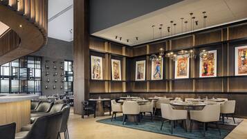 Un restaurant moderne avec de hauts plafonds, des boiseries et des œuvres d’art accrochées aux murs. Les tables sont disposées pour accueillir les clients, et un bar avec des tabourets est également à leur disposition.