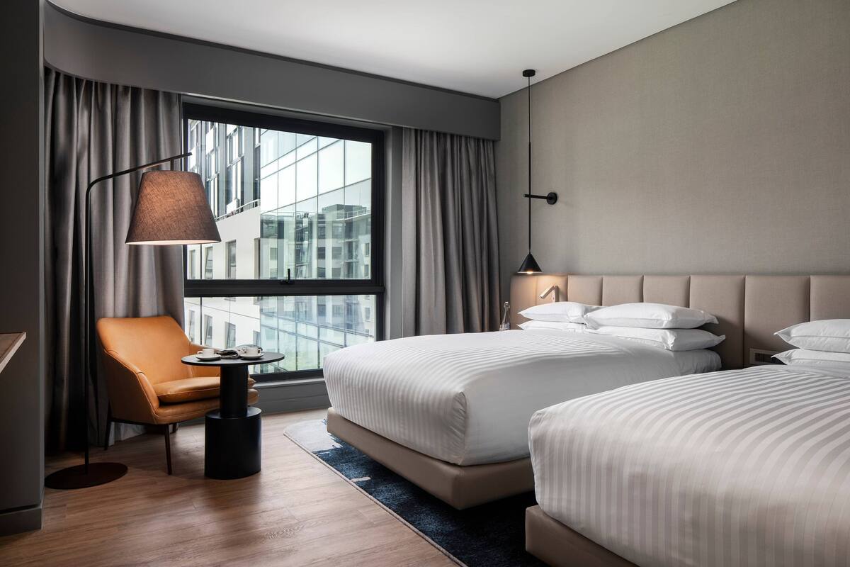 Une chambre d’hôtel avec deux lits, une chaise, une petite table et une lampe.