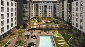 A modern apartment building with a rooftop pool, outdoor seating, and landscaped gardens.