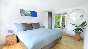 A bedroom with a bed, a nightstand, a potted plant, a window, and a wall-mounted mirror.