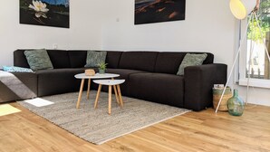 A modern living room with a dark brown sectional sofa, two small round tables, a grey rug, and two wall-mounted paintings.