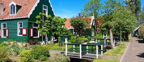 A green house with a red-tiled roof, a small pond, and a wooden bridge.