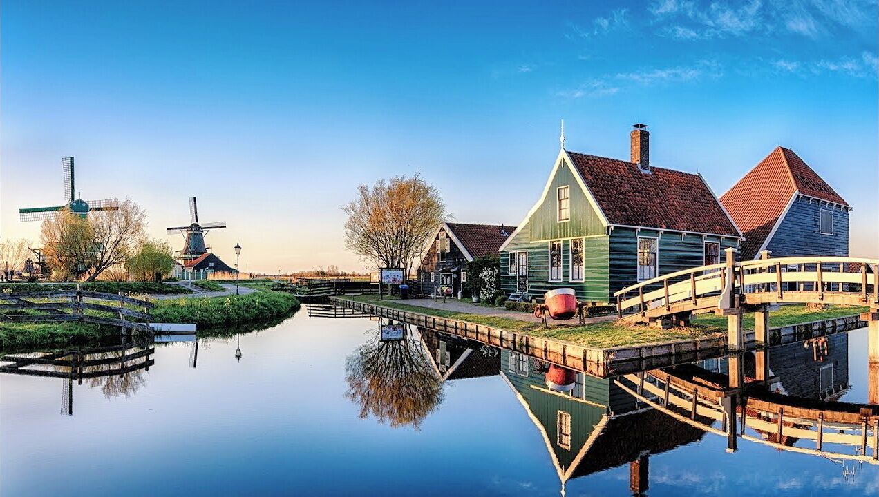 A canal with traditional windmills and wooden houses reflecting in the water.