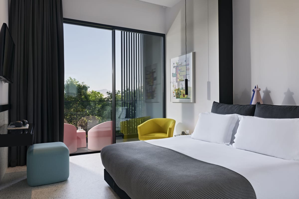 Habitación de hotel moderna con una cama grande, un escritorio, una silla y un balcón con vistas al verdor.