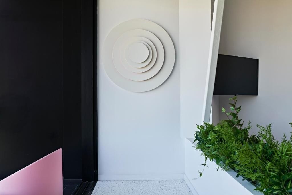 A modern interior with a white wall, a circular design, a black panel, a pink chair, and a green plant.