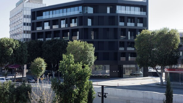 Un edificio moderno de varios pisos con fachada curva, amplios ventanales y un estacionamiento al frente.