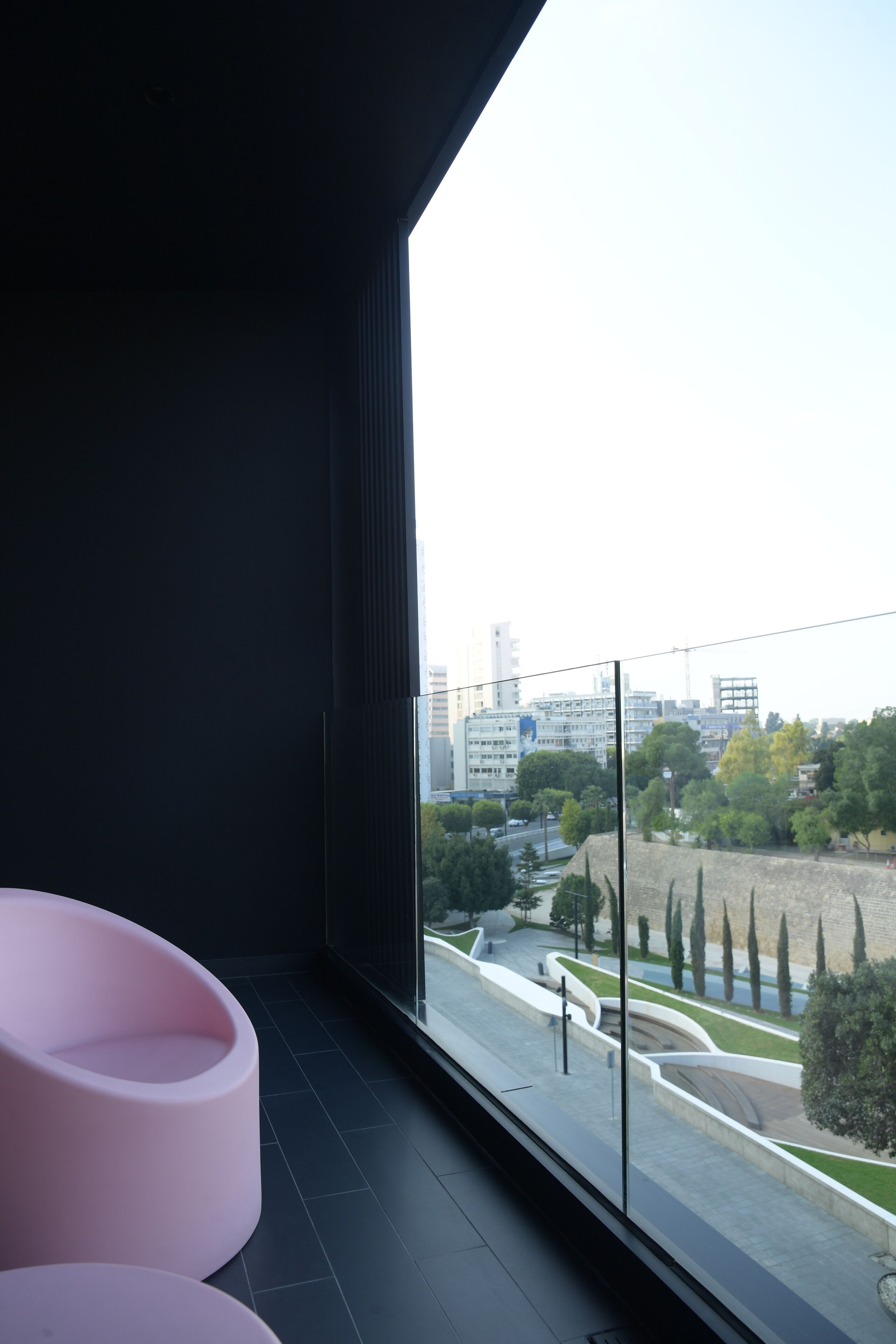 Une chambre moderne avec une grande fenêtre, un fauteuil rose et une vue sur le paysage urbain.