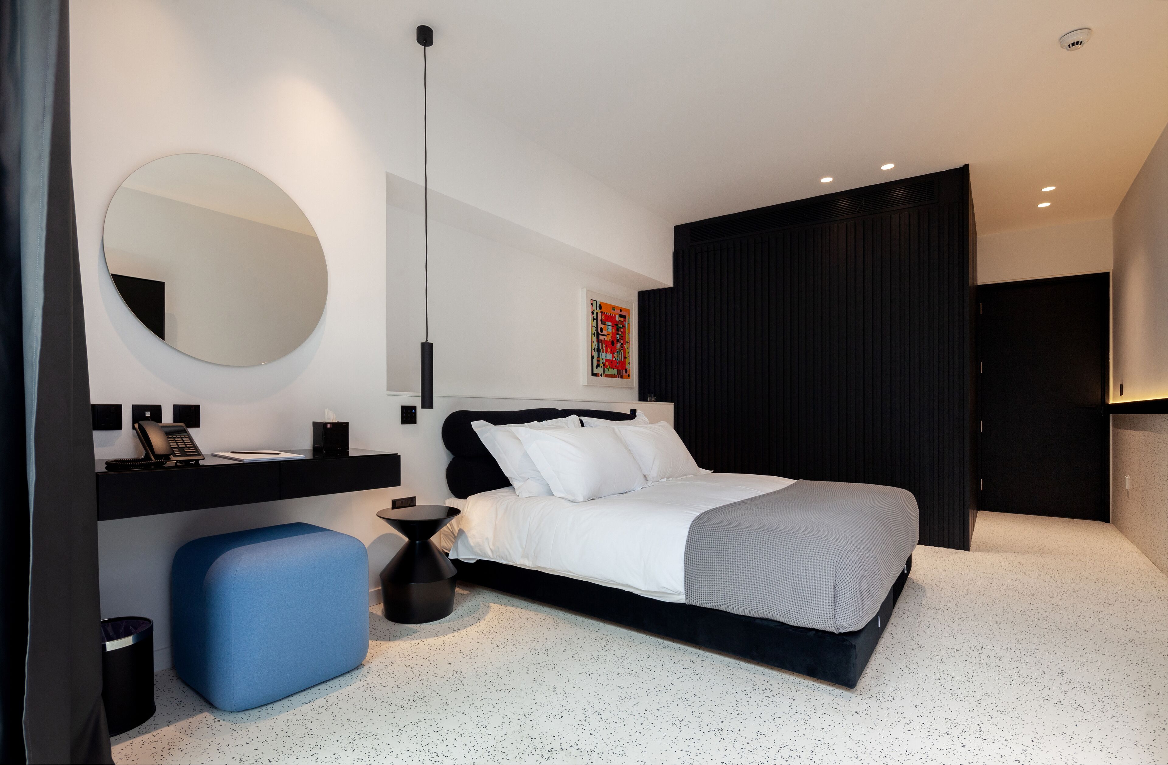 A modern bedroom with a bed, bedside tables, a mirror, and a blue ottoman.