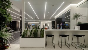 Un área de recepción moderna con un mostrador blanco, taburetes negros y plantas en macetas.