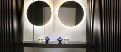 Une salle de bain moderne avec deux miroirs ronds, un meuble-lavabo avec un éclairage intégré et deux chaises blanches.