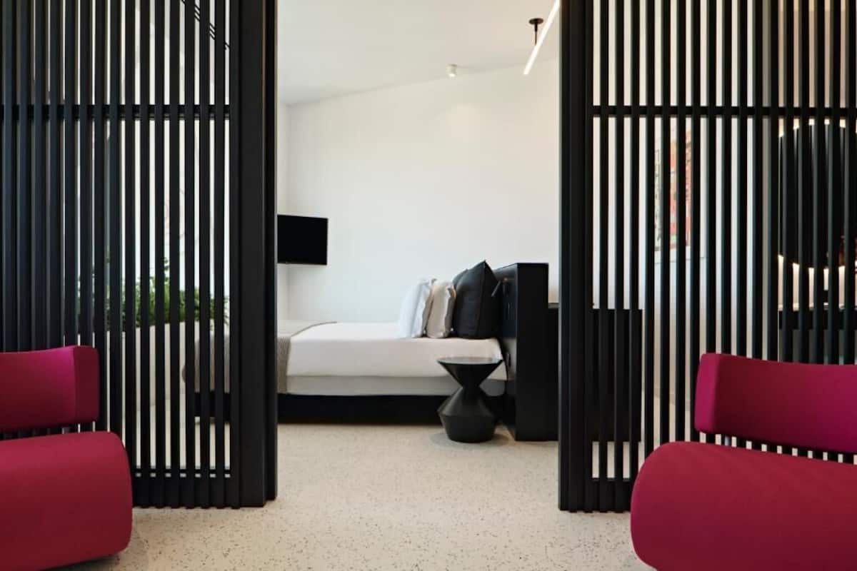 Un dormitorio moderno con una cama, un televisor negro y una silla roja.