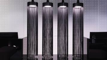 Three tall, narrow, black pendant lights with a reflective surface, hanging against a wall with evenly spaced, small, white dots.