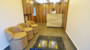 A reception area with a wooden reception desk, a blue carpet, and three beige armchairs. - Hotel Shreesh Kolkata (Kolkata)