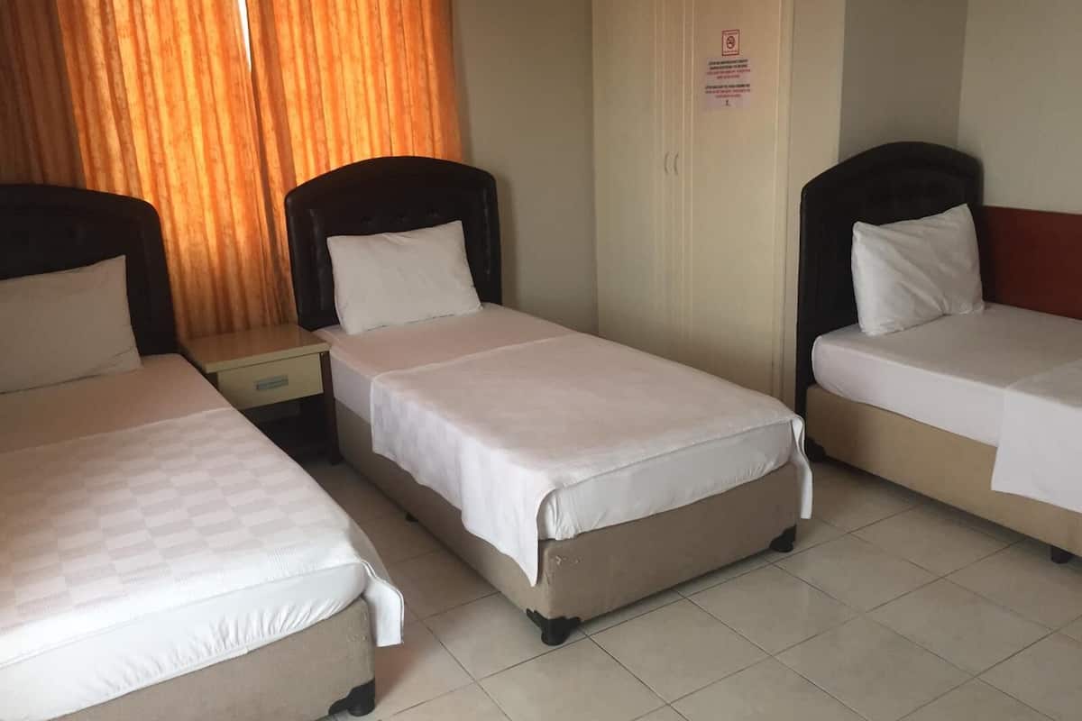 A hotel room with three single beds, a wardrobe, and a nightstand.