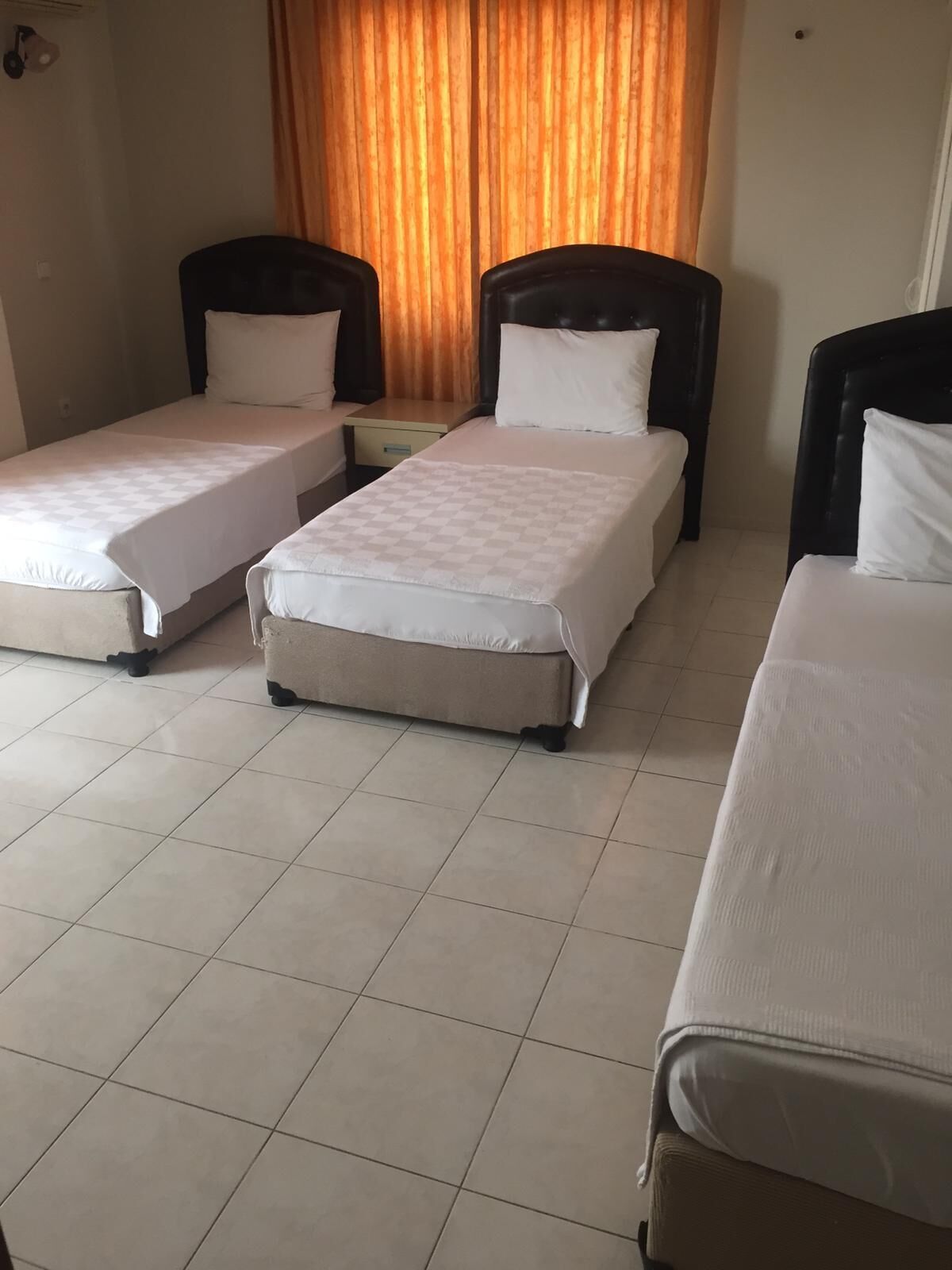 A hotel room with three single beds, a small table, and a curtain.