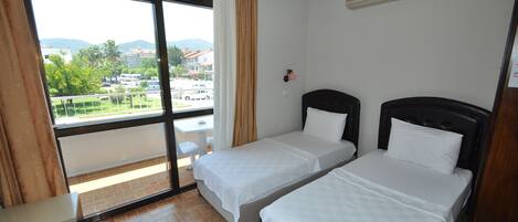 A hotel room with two beds, a window with curtains, a small table, and a view of the outside.