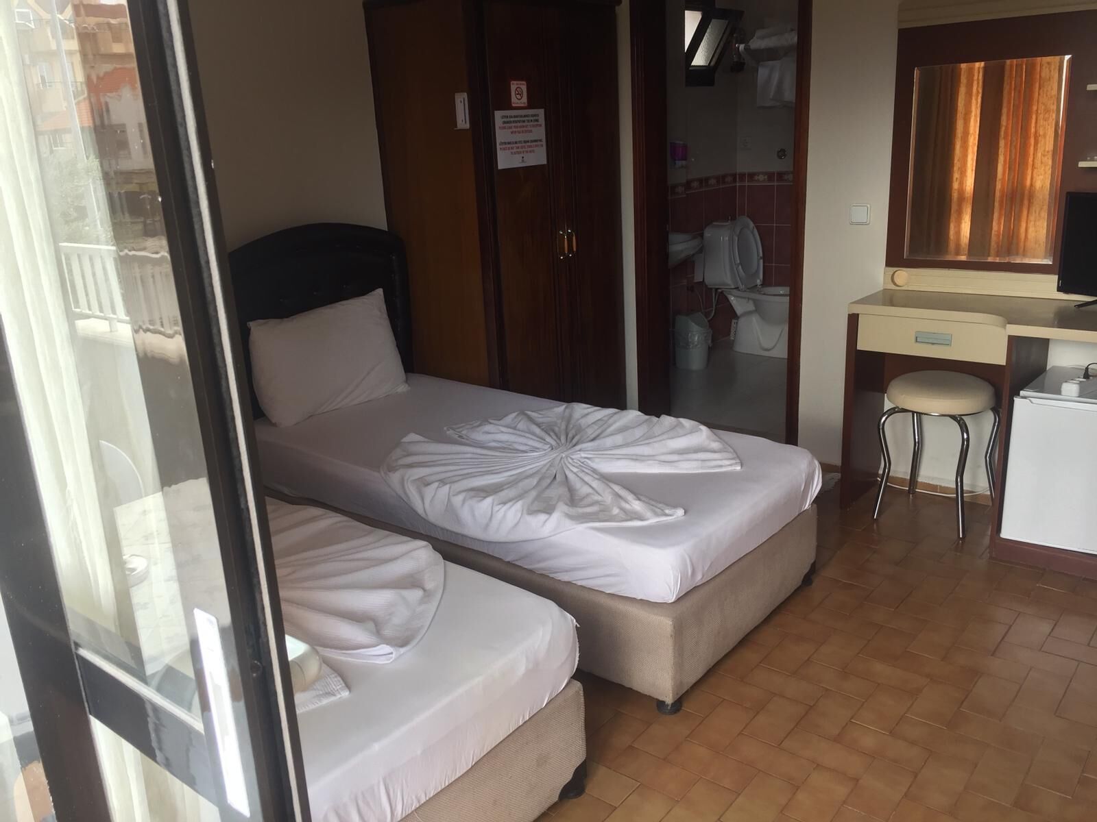 Habitación de hotel con dos camas individuales, un escritorio con silla y un baño visible a través de una puerta abierta.
