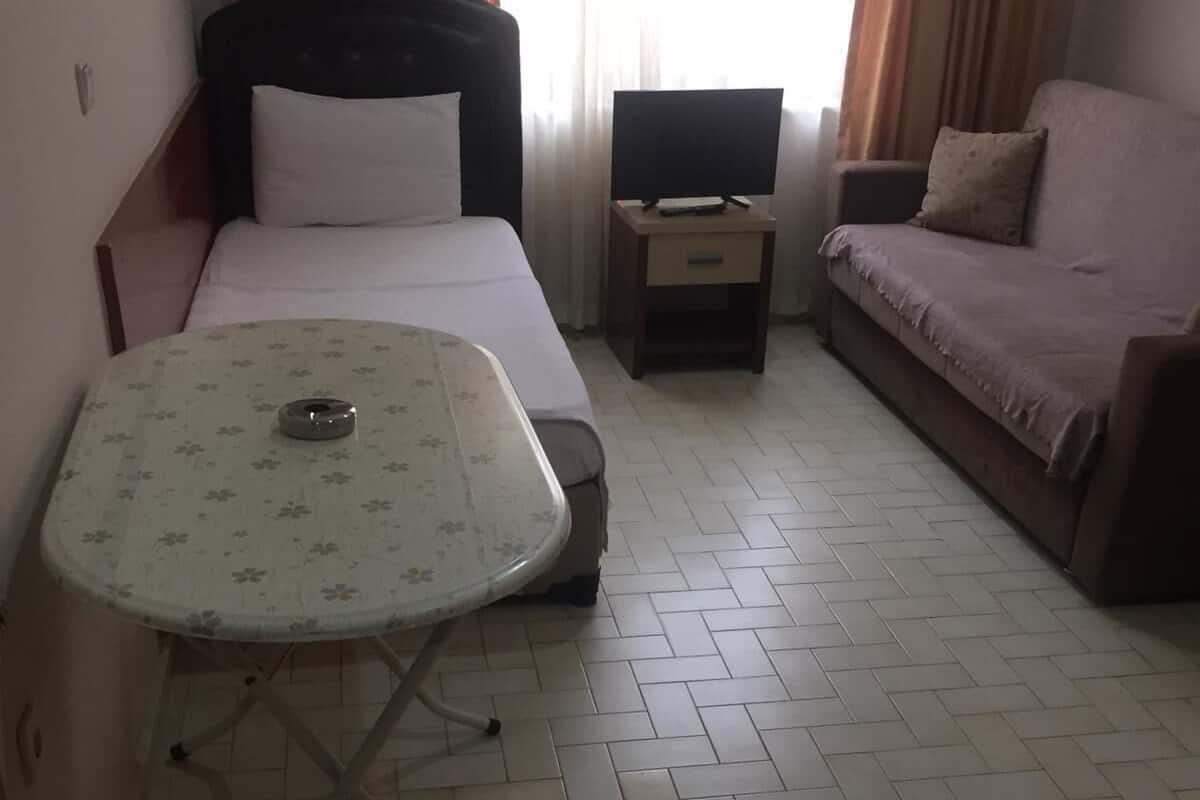 A hotel room with a bed, a small table, a TV, and a sofa.