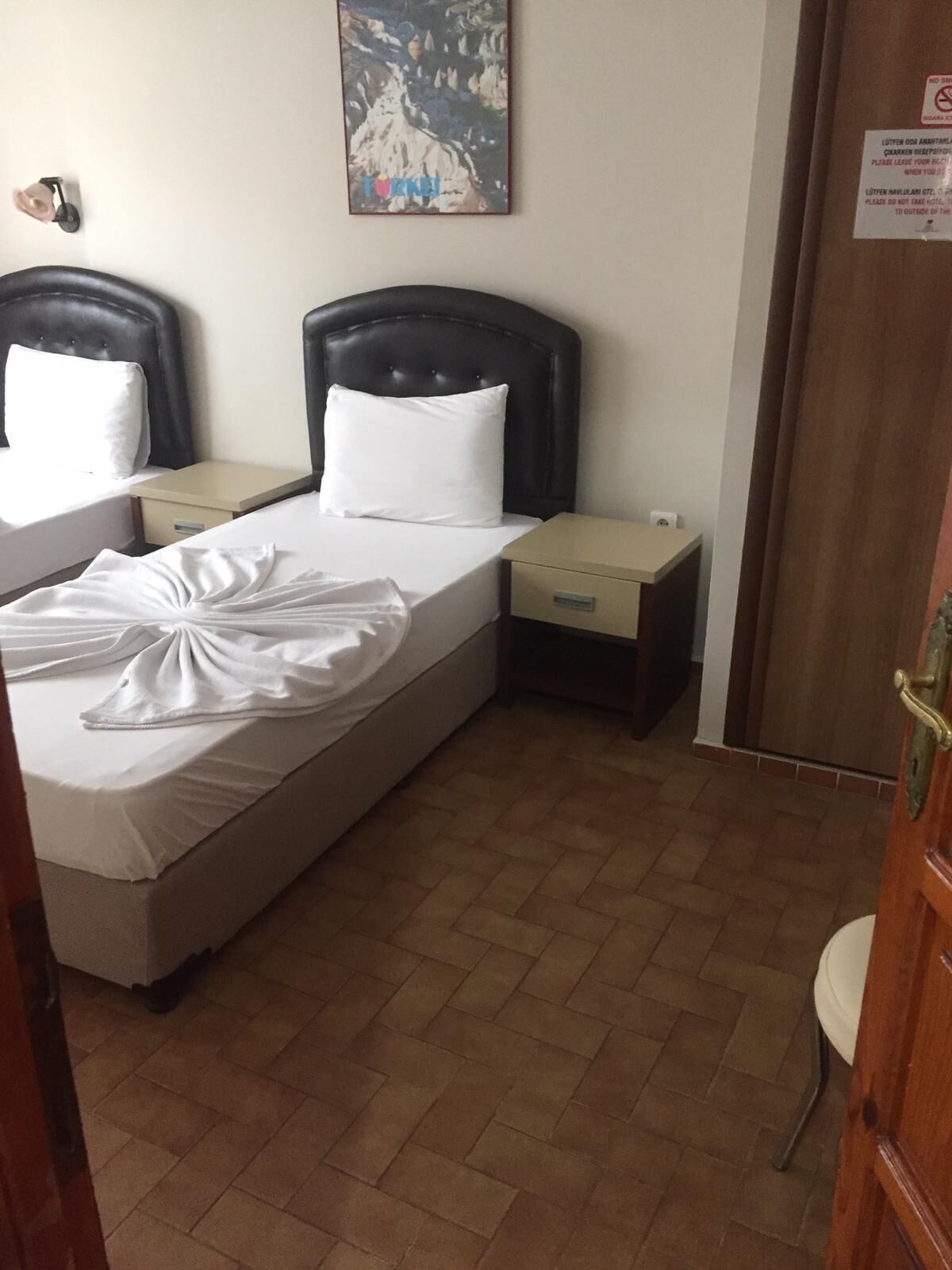 A hotel room with a bed, two nightstands, a small table, and a door.