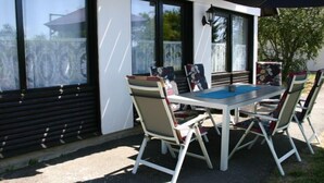 An outdoor patio with a white table and chairs, large windows, and a black umbrella.