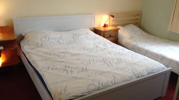 A double bed with a white headboard and footboard, two bedside tables, a nightstand with a lamp, and a wall with a framed picture.