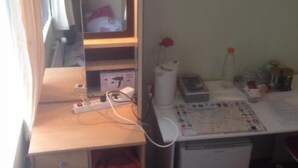 Una habitación pequeña con escritorio, un cesto de basura, radiador y espejo.