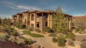A multi-story house with a stone facade, multiple balconies, and a landscaped driveway.
