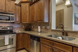 Una cocina con gabinetes de madera, electrodomésticos de acero inoxidable, encimera de granito y pileta doble.