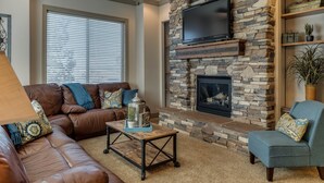 A living room with a stone fireplace, a flat-screen TV, a brown leather couch, and a ceiling fan.