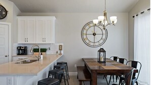 A modern kitchen with white cabinets, a large island with a sink, and a dining area with a wooden table and chairs. - Spacious Villa 5 minutes to Lake State park by Redawning (Washington)