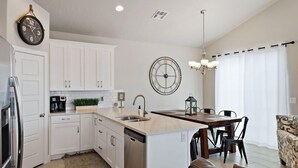 A modern kitchen with white cabinets, a built-in dishwasher, a coffee machine, and a clock on the wall. - Spacious Villa 5 minutes to Lake State park by Redawning (Washington)