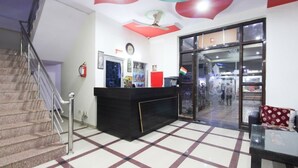 Un hall de hotel con mostrador de recepción, una escalera y un puerta de cristal que da al exterior.