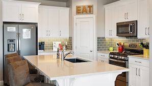 A modern kitchen with white cabinetry, a stainless steel refrigerator, a built-in microwave, a gas stove, and a sink with a faucet. - Sunshine Serendipity 4 Bedroom Apts by RedAwning (Washington)