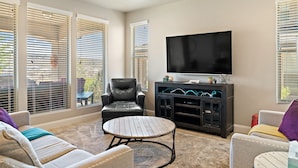 A living room with a leather chair, a round coffee table, a flat-screen TV, and a cabinet with decorative items. - Sunshine Serendipity 4 Bedroom Apts by RedAwning (Washington)