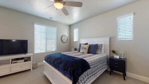 A bedroom with a bed, a TV, a ceiling fan, and a nightstand.