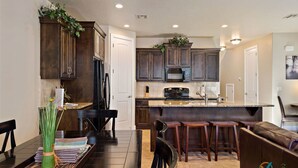 A modern kitchen with dark wooden cabinets, a central island with stools, and a dining area with a table and chairs. - Bike-on-inn 3 Bedroom Apts by RedAwning (Washington)