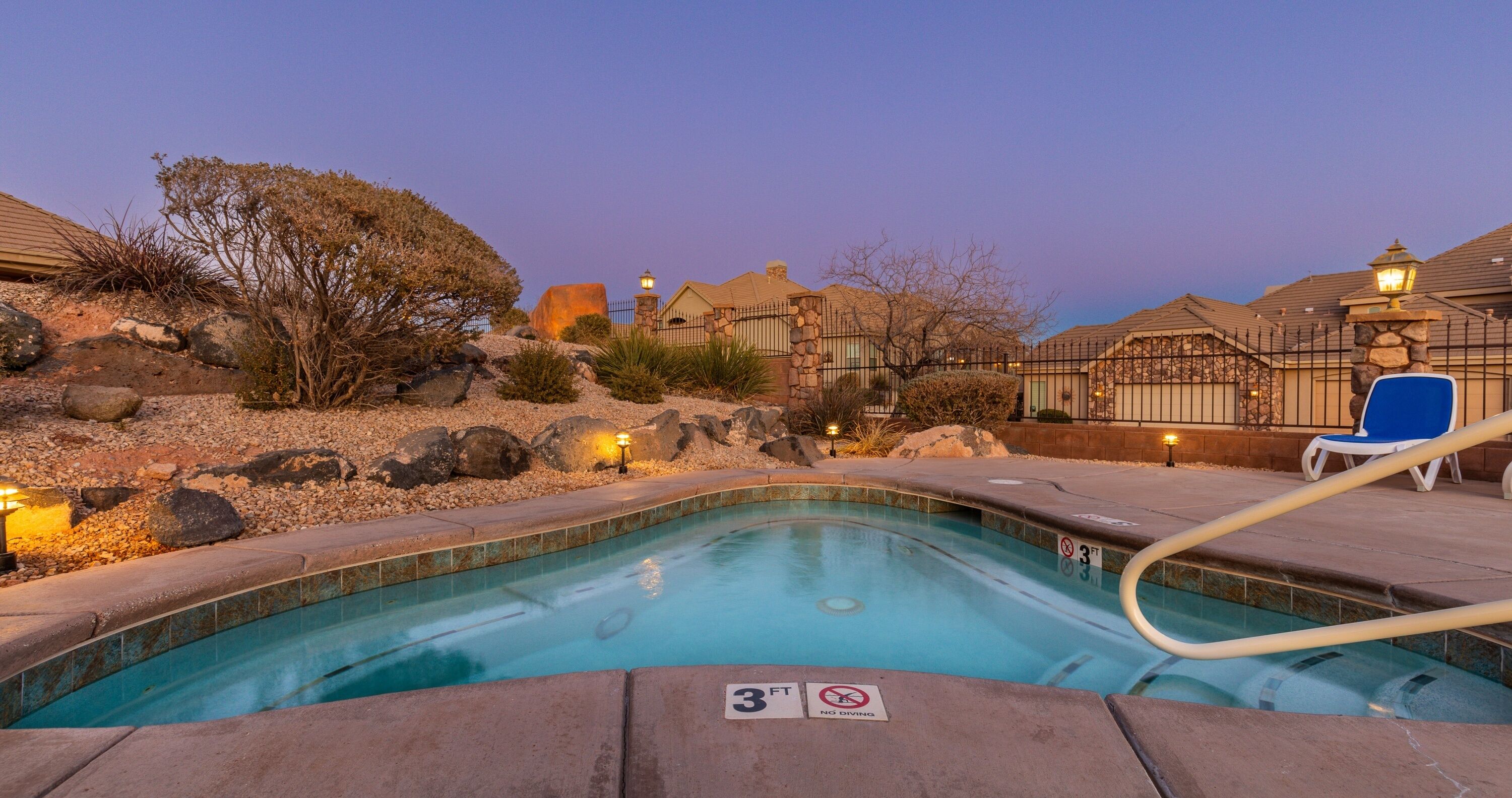 A swimming pool with a 3 ft depth limit sign, surrounded by a stone wall, with a blue chair and a lamp post in the background.