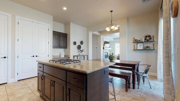 Una cocina moderna con armarios oscuros, encimera de granito y comedor con mesa y sillas de madera.