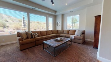 Una sala de estar con un sofá modular, una mesa de centro y ventanas amplias con persianas.
