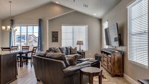 A spacious living room with a leather sofa, a coffee table, and a TV. There is a dining area with a table and chairs, and a kitchen area with a counter and cabinets. - Desert Edge 3 Bedroom Townhouse by RedAwning (Washington)